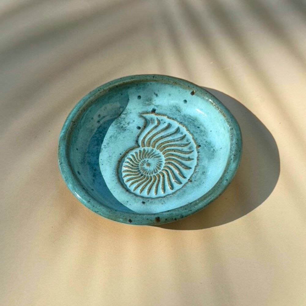 Turquoise ceramic dish with a shell pattern on a beige surface